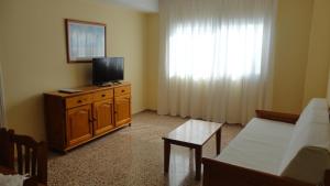 a living room with a tv on a wooden dresser with a couch at Apartamentos Cala Llonga in Cala Llonga