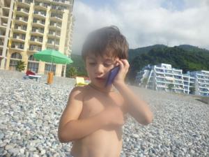 a young boy talking on a cell phone at the beach at Апартаменты свидом наморе Гонио in Kvariat'i