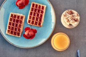 a plate with waffles and strawberries and a bowl of cereal at Elysian Santorini in Oia