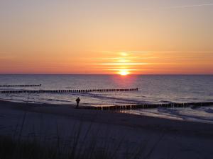 ツィングストにあるFerienwohnung am Strandの夕日を見ながら浜辺に立つ者