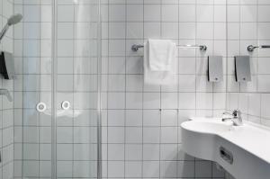 a white tiled bathroom with a shower and a sink at Comfort Hotel Børsparken in Oslo