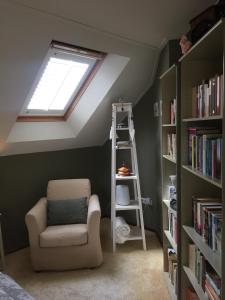 um quarto no sótão com uma janela, uma cadeira e estantes em B&B De Koraal em Emmen