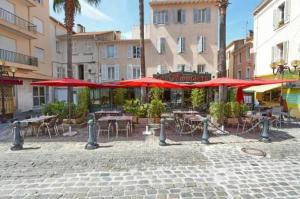 eine Terrasse mit Tischen, Stühlen und roten Sonnenschirmen in der Unterkunft Les Palatines Penthouse in Saint-Raphaël