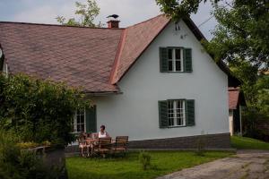 a woman sitting at a table in front of a white house at Ferienhaus Vogeljager in Leutschach
