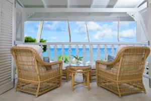 a porch with wicker chairs and a table and the ocean at Cobblers Cove - Barbados in Saint Peter