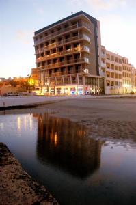 a building on the beach with a reflection in the water at Water's Edge Hotel in Birżebbuġa