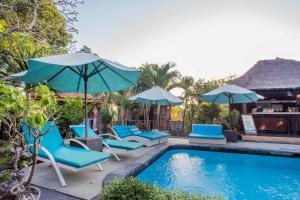a swimming pool with blue chairs and umbrellas next to a pool at Lotus Garden Huts in Nusa Lembongan
