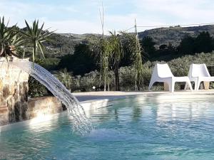 una piscina con 2 sillas blancas y una fuente de agua en La Suite Di Segesta en Calatafimi