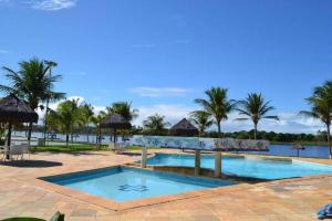 a swimming pool with palm trees and a body of water at Guarajuba Summer House in Guarajuba