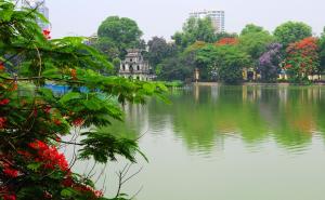 a lake in a park with trees and buildings at Hanoi Golden Charm Hotel in Hanoi