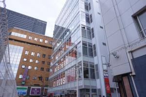 a tall glass building on a city street with buildings at Book And Bed Tokyo Shinjuku in Tokyo