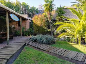 a garden with palm trees and a wooden walkway at Saltycrax Backpackers and Surf Hostel by CURIOCITY in Bloubergstrand