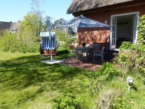 eine Terrasse mit einem Tisch und einem Sonnenschirm im Hof in der Unterkunft Ferienwohnung *Reethuk* in Norddorf
