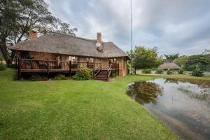 une maison au toit de chaume à côté d'un étang dans l'établissement Kruger Park Lodge Unit No. 277, à Hazyview