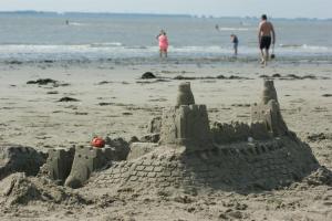 un château de sable sur la plage avec des gens dans l'eau dans l'établissement Do's Chalets, à Baarland