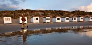 a man walking on a beach with beach huts at Løkken Strand Camping in Løkken
