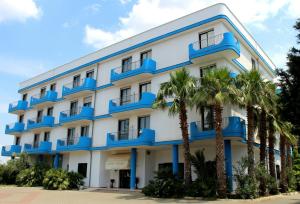 a large white building with blue balconies and palm trees at Hotel Villaggio Aurora in San Pietro in Bevagna