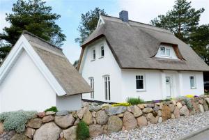 a white house with a gray roof and a stone wall at Idylle unterm Reet - Reetdachhäuser am Walde in Trassenheide