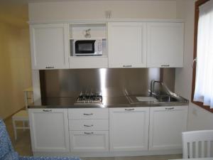 ピンツォーロにあるSillia Appartamentiの白いキャビネット、シンク、電子レンジ付きのキッチンが備わります。
