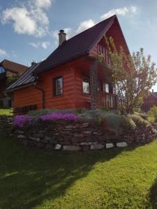 a log house with a stone wall and purple flowers at Chalúpka u Babičky in Ždiar