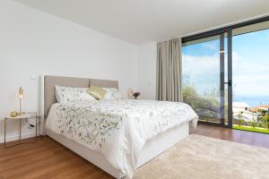 a white bedroom with a bed and a large window at Casa Melinho Lotus in Calheta