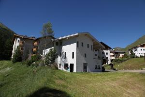ein weißes Gebäude auf einem grasbewachsenen Hügel mit Häusern in der Unterkunft Apart Foresta in Samnaun