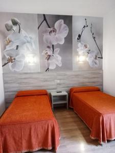twee bedden in een kamer met oranje lakens en bloemen aan de muur bij Hotel Yeste in Yeste