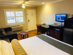 a room with a bed and a desk with a television at Dynasty Suites Hotel in Riverside