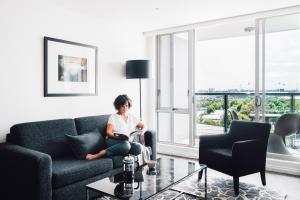 a woman sitting on a couch reading a book in a living room at Quay West Suites Melbourne in Melbourne