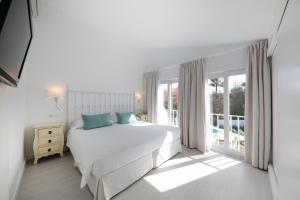 a white bedroom with a large bed and a window at Hotel La Pergola Mallorca in Port d'Andratx