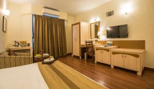 a hotel room with a bed and a desk with a television at Hotel Park Central Koregaon Park in Pune