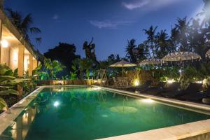 una piscina por la noche con sillas y sombrillas en Gangga Blessta Hotel, en Ubud