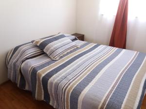 a bed with a striped blanket and two pillows at Cabañas M y M Frutillar in Frutillar