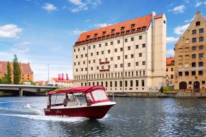 a boat in the water in front of a building at Qubus Hotel Gdańsk in Gdańsk