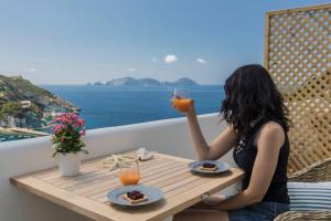 Eine Frau, die mit einem Glas Saft am Tisch sitzt. in der Unterkunft Maridea Casa Vacanza- Le Alcove sul Mare Suites in Ponza