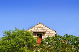 an old stone building with a red window and trees at Old Small Stone House in Korčula