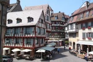 a group of buildings in a street with tables and umbrellas at Entre douceur et délicatesse in Colmar