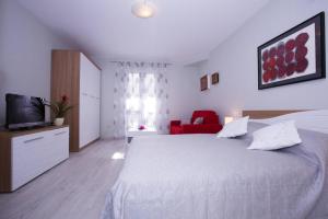 a white bedroom with a bed and a red chair at Apartments Daisy in Dubrovnik