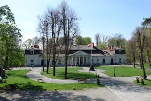 uma grande casa branca com árvores em frente em Gościniec Dworski w Ropie - Pokoje gościnne em Ropa