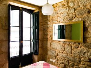 a bedroom with a stone wall with a window and a mirror at Santiaguiño 2 in Padrón