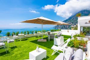 eine Terrasse mit weißen Stühlen, Tischen und einem Sonnenschirm in der Unterkunft Villa Pietra Santa in Positano