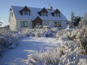 a white house in the snow with tall grass at The Lovecroft Guest House in Laide