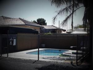 a fence with a swimming pool in front of a house at Country Roads Motor Inn in West Wyalong