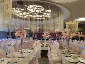 une salle de banquet avec des tables et des chaises blanches ainsi qu'un lustre dans l'établissement Van Royal Hotel, à Erbil