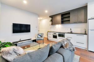 a living room with a gray couch and a kitchen at Designer Styled City Apartment with Carpark in Auckland