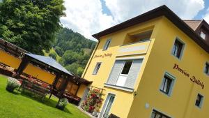 a large yellow building on a hill with trees at Pension & Ferienwohnung Dullnig in Gmünd in Kärnten