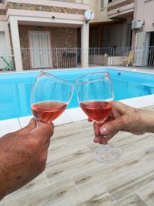 Due persone che portano bicchieri di vino di fronte a una piscina di Casa vacanze "La Caldosa" a Badesi