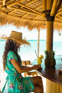 Eine Frau, die an einem Tisch am Strand mit einem Drink sitzt. in der Unterkunft Island View Bar & Bungalow in Gili Air