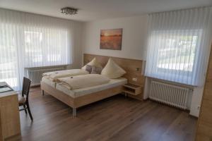 a bedroom with a bed and a desk and windows at Gästehaus Aßlschwang in Freystadt