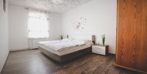 a white bedroom with a bed and a wooden floor at Apartma Trebušca in Dolenja Trebuša